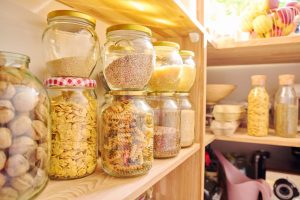 Petit placard bien organisé avec des bocaux, boîtes et provisions rangés sur plusieurs étagères.