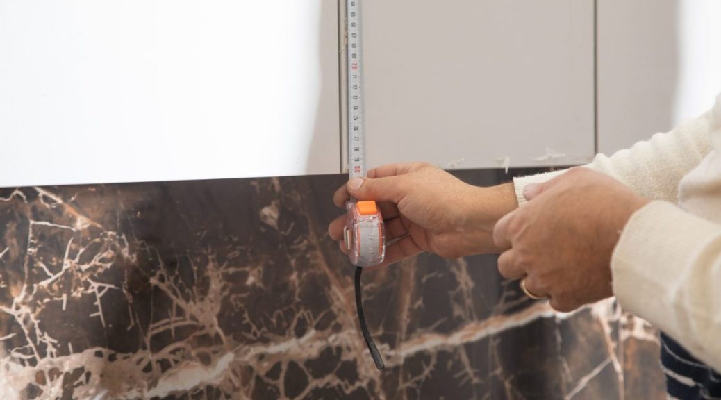 Locataire installant une protection murale derrière une plaque de cuisson dans une cuisine.